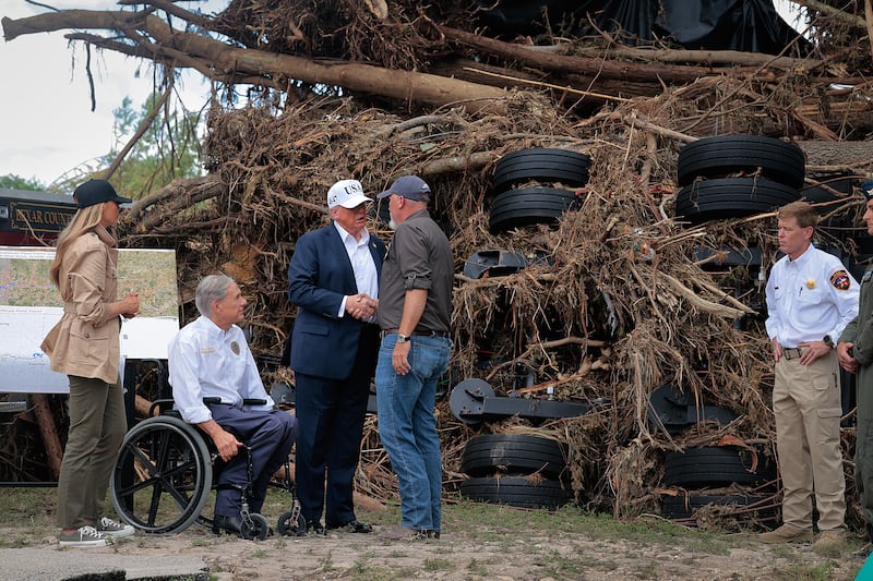 Donald Trump, first lady Melania Trump and Texas Governor Greg Abbott . Trump is shaking hands with a tall man in front of debris.