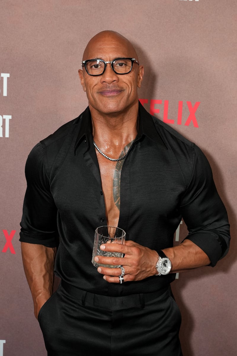 Dwayne Johnson holds a drink at the 2026 roast of Kevin Hart, wearing a black shirt and black pants.