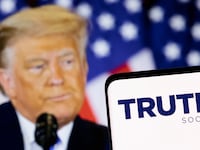 The Truth social network logo is seen on a smartphone in front of a display of former U.S. President Donald Trump.