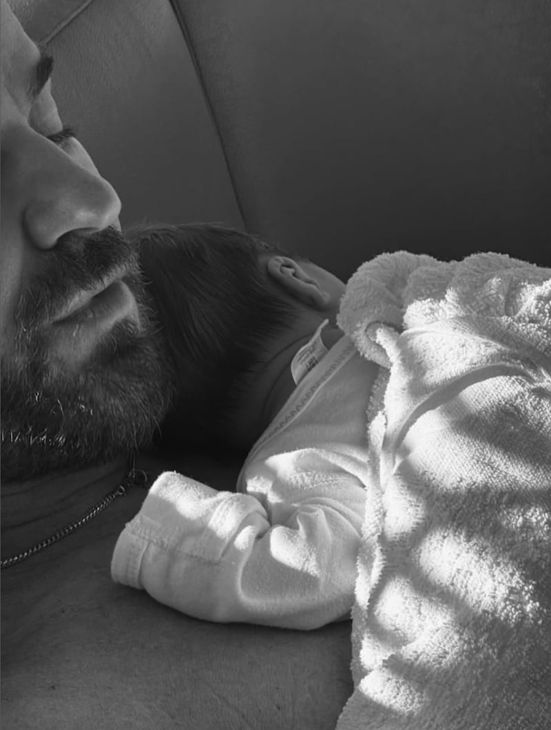 Black and white photo of Justin Theroux holding a baby on his bare chest.