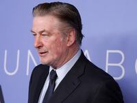 Alec Baldwin, wearing a suit and tie, stares forward at an event.