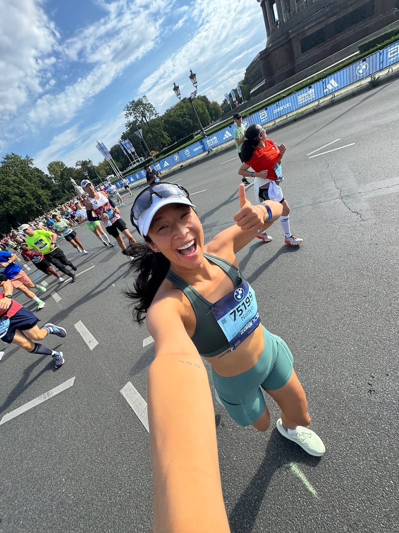 Athlete Nadya Okamoto poses for a selfie while giving a thumbs-up and running a race.