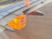 A view from a plane window shows a fireball bursting out from below the jet's wing.