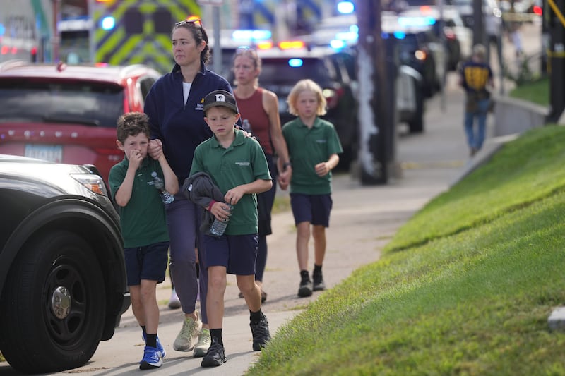 Parents walk with their children away from the scene after the shooting at Annunciation Church on Wednesday morning.