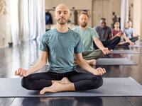 Group of people sitting on mats in lotus padmasana pose. Multiracial group of men meditating in sitting yoga pose in yoga class, mindfulness and meditation.