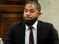 Jussie Smollett, wearing a suit with a face mask pulled down on his chin, listens in a courtroom.