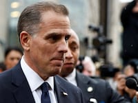 Hunter Biden, wearing a suit, walks past reporters’ microphones.