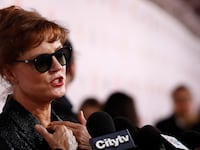 Susan Sarandon, wearing sunglasses, speaks into a microphone during an interview.