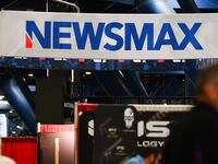 Signage for the Newsmax conservative television broadcasting network is displayed at a broadcast TV booth at the National Rifle Association