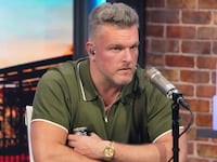 Pat McAfee sits in a green polo while sitting in front of a microphone for his show.