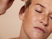 Young beautiful woman with closed eyes applying face serum with pipette