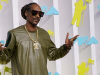 Snoop Dogg has his hands up while he poses for a photo outside an event.