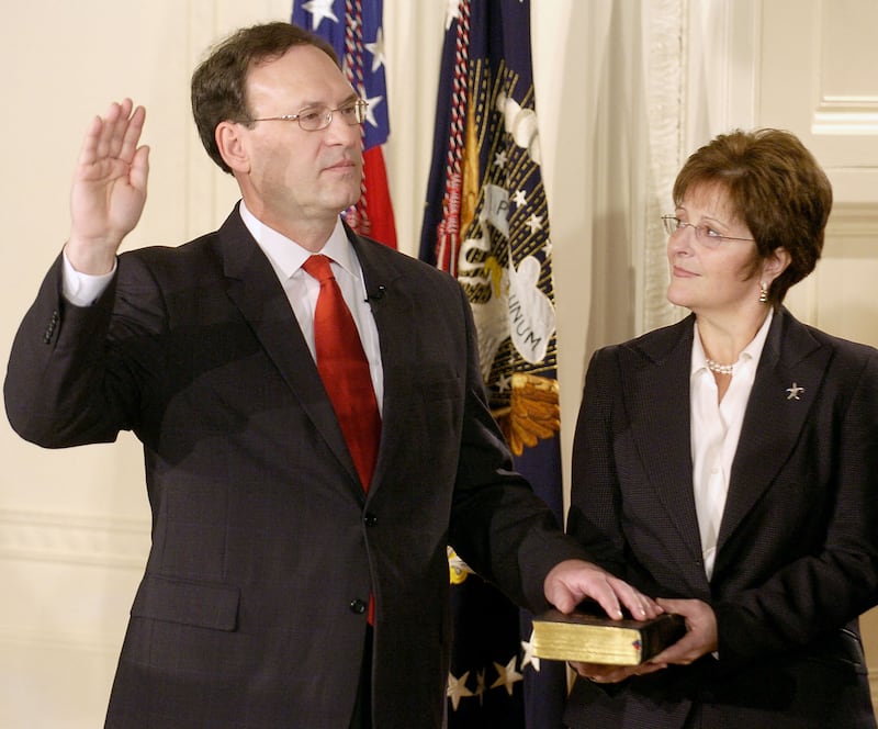 Samuel Alito raises his hand as he is sworn into the Supreme Court. His wife, Martha Ann holds the bible next to him.