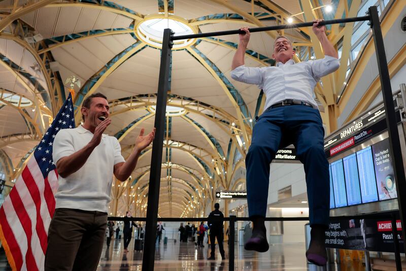 Influencer Dr. Paul Saladino watches U.S. Transportation Secretary Sean P. Duffy do pull-ups after a press conference discussing the launch of the "Make Travel Family Friendly Again" campaign at Ronald Reagan Washington National Airport