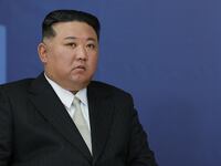 North Korean leader Kim Jong un sits next to a flag.