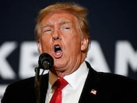 Donald Trump, wearing a suit and tie, speaks on stage during an event.