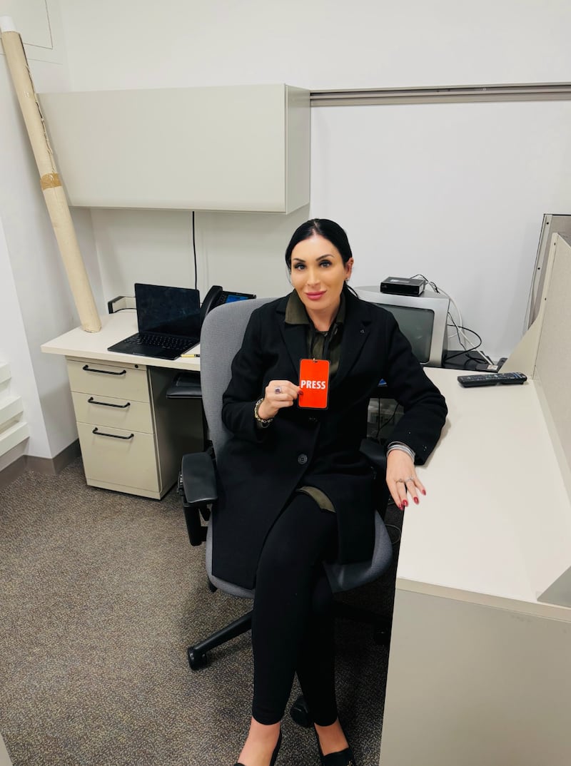 Laura Loomer sits at office desk holding a press pass.