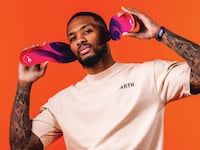 Damian Lillard standing in front of an orange background while holding two Move Insoles up to his ears.