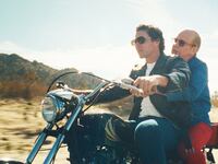 Vito Scnabel and Tom Hollander ride a motorcycle in a still from ‘Feud: Capote vs The Swans’