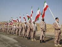 Members of the Islamic Revolutionary Guard Corps (IRGC) stand in a row carrying flags at a military drill