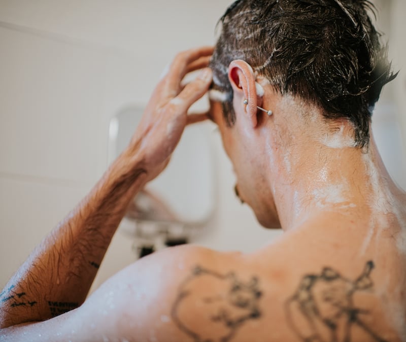 A man, turned away, rinses shampoo out of his hair in the shower.