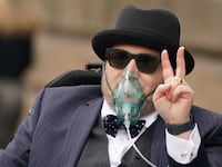Nicholas Rossi throws up a peace sign as he is wheeled out of court in 2022.