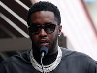 Sean Combs speaks behind a microphone and clear podium outdoors.