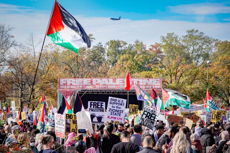 A Palestinian flag waves as protesters hold signs and call for a Israeli ceasefire.