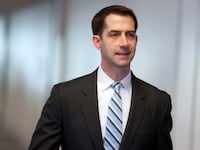 Tom Cotton smirks as he walks in the Senate, wearing a suit and tie.