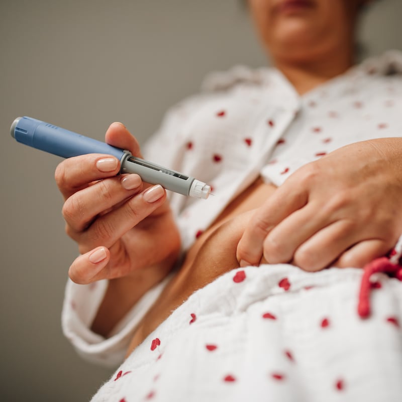Close-up of woman administering insulin shot to stomach using injection pen.