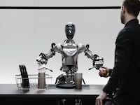 A robot sits at a table with a human standing in front of it
