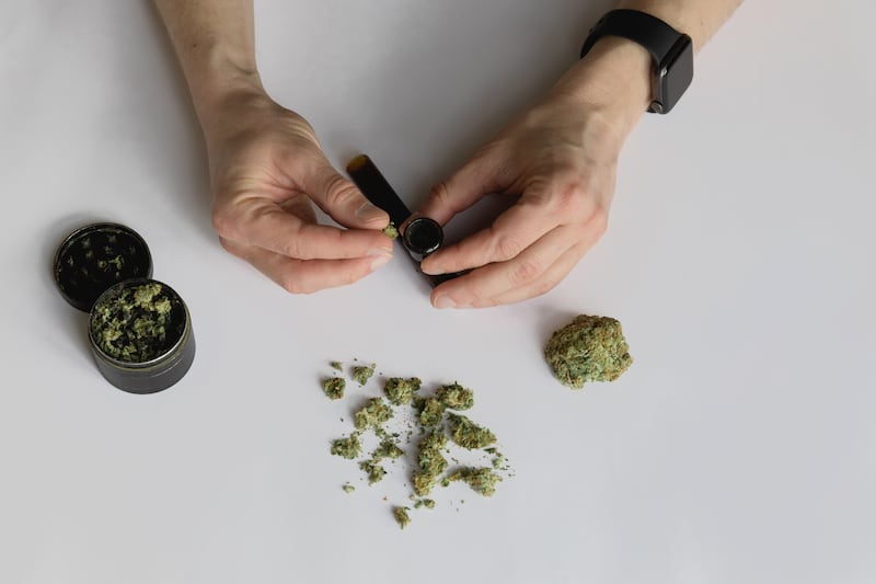 Man’s hand with smart watch filling smoking glass pipe with marijuana. Weed and grinder on white background.