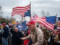 Ray Epps, in the red Trump hat, center, gestures to a line of law enforcement officers, as people gather on the West Front of the U.S. Capito