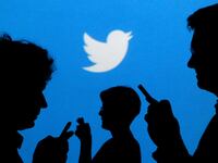 People holding mobile phones are silhouetted against a backdrop projected with the Twitter logo.