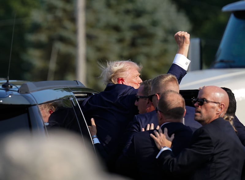 Former president Donald Trump raises his arm as he's helped into a Secret Service vehicle after an assassination attempt