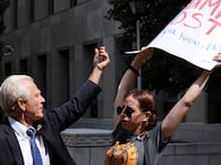 Peter Navarro, a White House economic adviser under former U.S. President Donald Trump, tries to grab a protestors sign while speaking to reporters