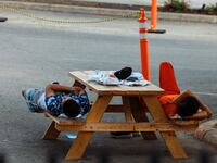 A photo of migrants laying on a bench outside the City of San Antonio Migrant Resource Center.