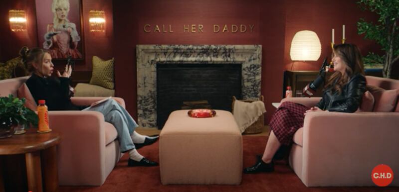 Call Her Daddy host Alex Cooper and Monica Lewinsky sit on opposite-facing pink couches during an interview.