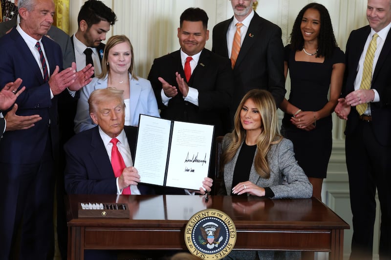 WASHINGTON, DC - NOVEMBER 13: U.S. President Donald Trump, joined by first lady Melania Trump, members of his administration and foster care advocates, holds up a copy of the "Fostering the Future" executive order after signing the order in the East Room of the White House on November 13, 2025 in Washington, DC. The executive order, championed by first lady Melania Trump, works to expand opportunities for education, career development, housing and other resources for youth transitioning from foster care to adulthood. (Photo by Anna Moneymaker/Getty Images)