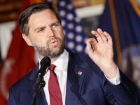 JD Vance raises his left hand while speaking at a campaign event.