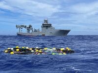 Bags of cocaine float in the Pacific Ocean as a boat floats in the background.
