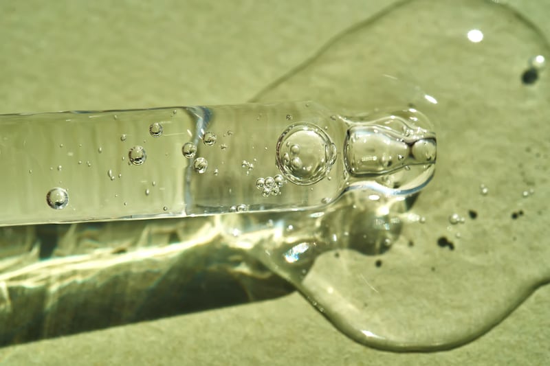 Pipette with cosmetic serum with a drop of CBD gel on a green background.