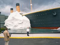 A still from “How to with John Wilson” that shows John WIlson in the foreground looking at a replica of the Titanic