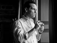 Andrew Scott holds a camera in a window in a still from 'Ripley'