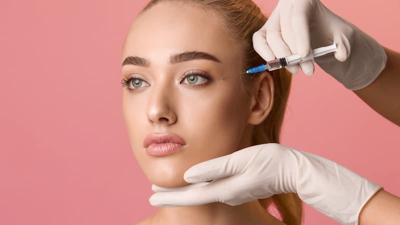 Young woman getting beauty injection near eyes, pink background