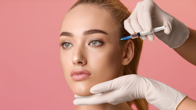 Young woman getting beauty injection near eyes, pink background