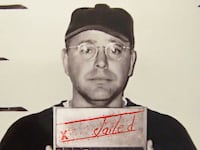 Tim Walz in a mugshot wearing a baseball cap and glasses