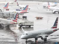 A ground crew de-ices an Embraer ERJ-175 American Eagle passenger plane (L) at LaGuardia Airport in New York on February 22, 2026. A fast-developing storm is threatening to pummel the US East Coast with a foot or more of snow beginning Sunday, bringing Mother Nature's wrath to a region that only just dug out from a previous winter wallop. Meteorologists issued blizzard warnings for New York and parts of at least six states, warning Saturday that heavy snow and gale-force winds are forecast to slam all major cities along the densely populated Interstate 95 northeast corridor, including Philadelphia, Boston and even Washington further south. (Photo by CHARLY TRIBALLEAU / AFP via Getty Images)