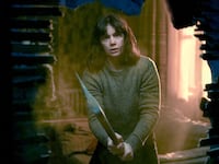 Ruth Wilson holds an axe and peers through a hole in the wall in a still from ‘The Woman in the Wall’