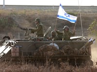 Israeli soldiers ride an armored vehicle topped with an Israeli flag.